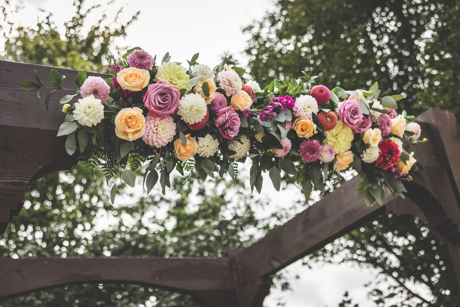 Elegant floral arch with pink and white roses decorates an outdoor wedding ceremony space.