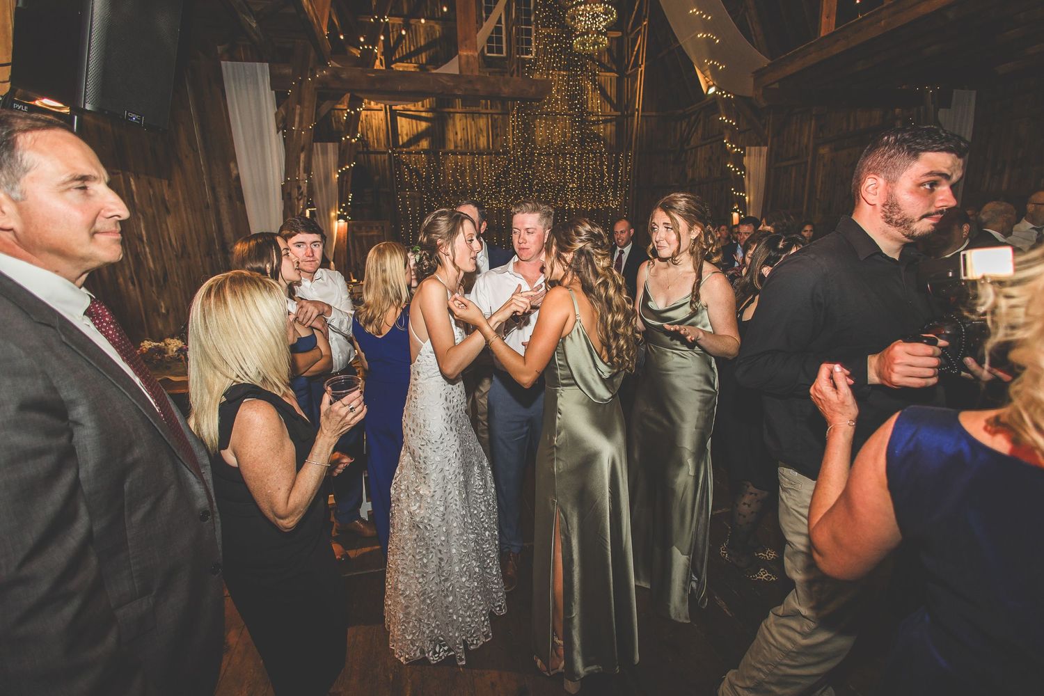 Wedding reception guests dancing and mingling in a warmly lit rustic barn setting.