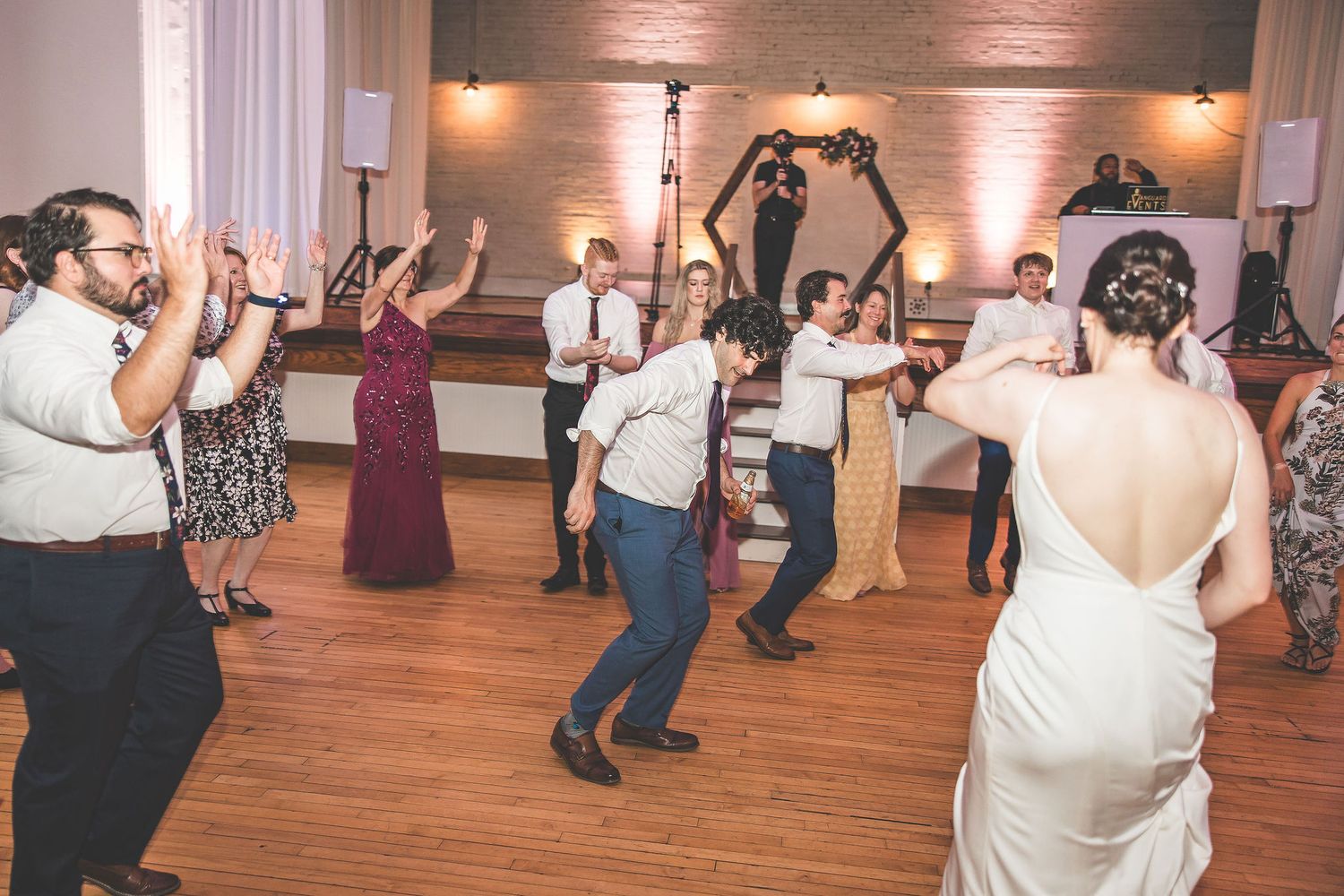 Wedding guests dancing and celebrating together at an indoor reception venue.