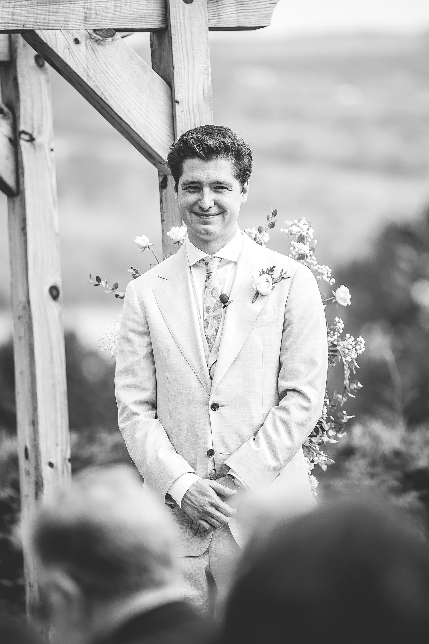 Black and white photo of outdoor wedding ceremony under decorated wooden pergola.