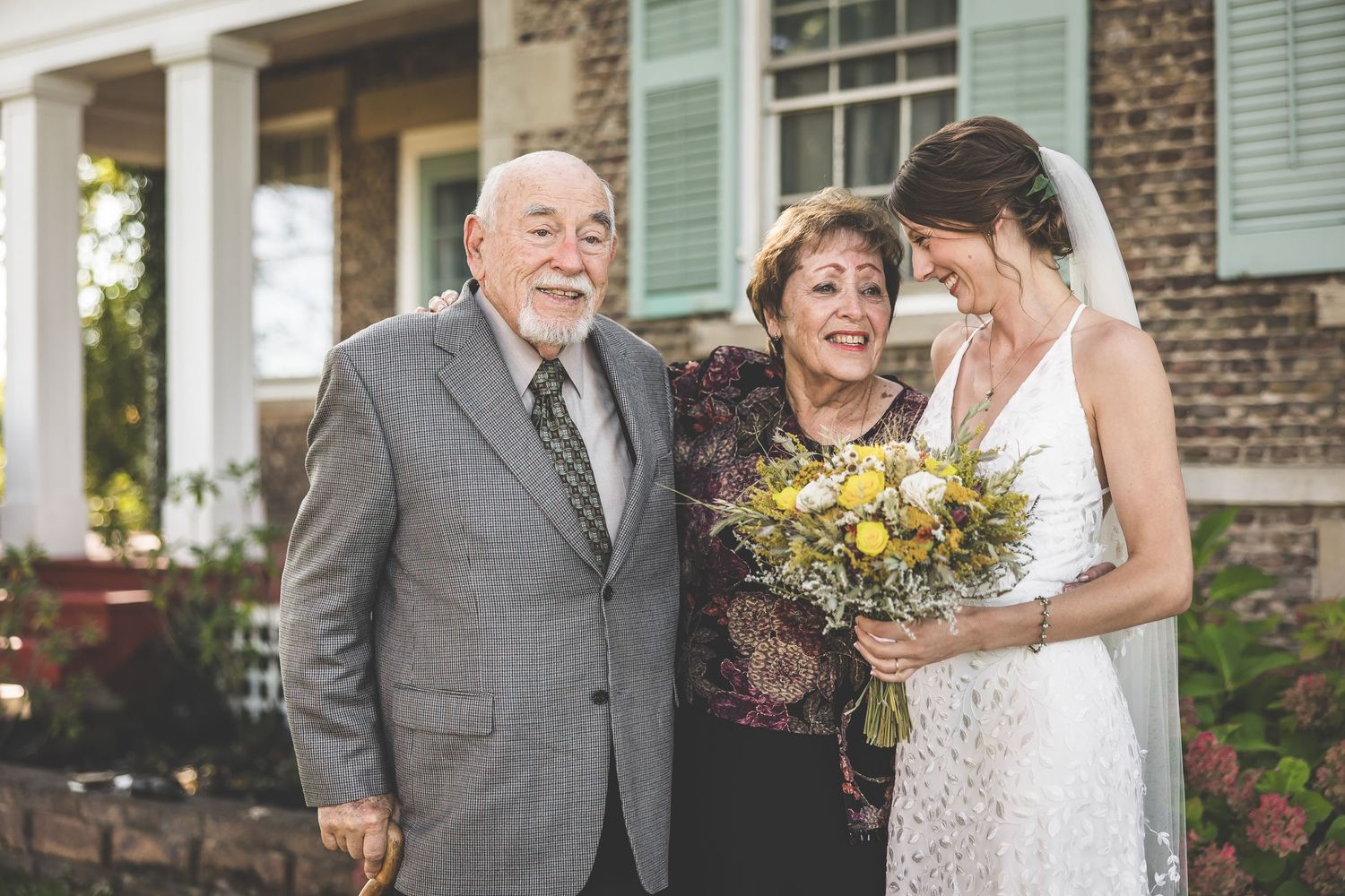 Emotional moment captured during wedding photos outside historic brick building with green shutters.