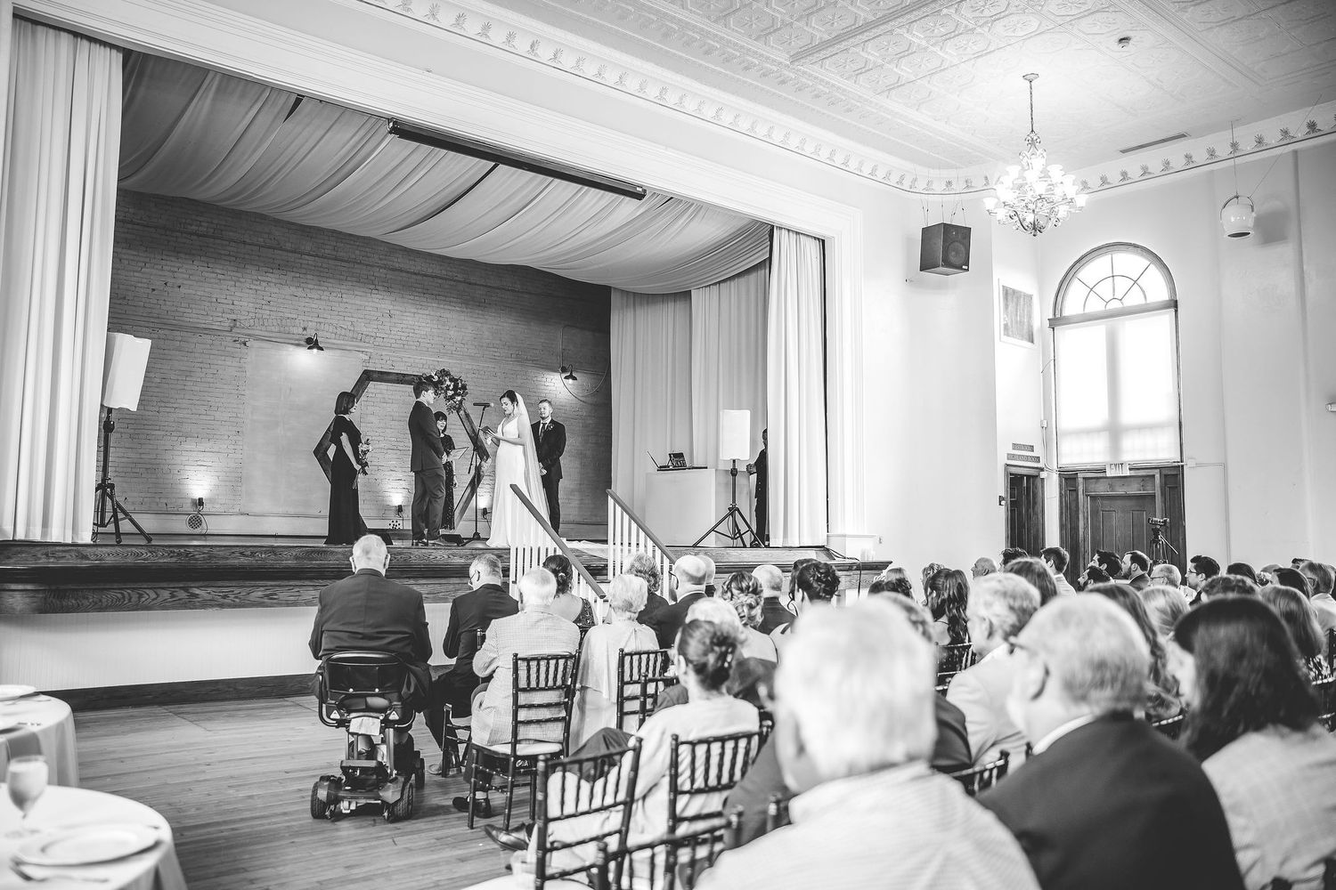 Black and white panorama of a wedding venue interior with rows of chairs and elegant crown molding.