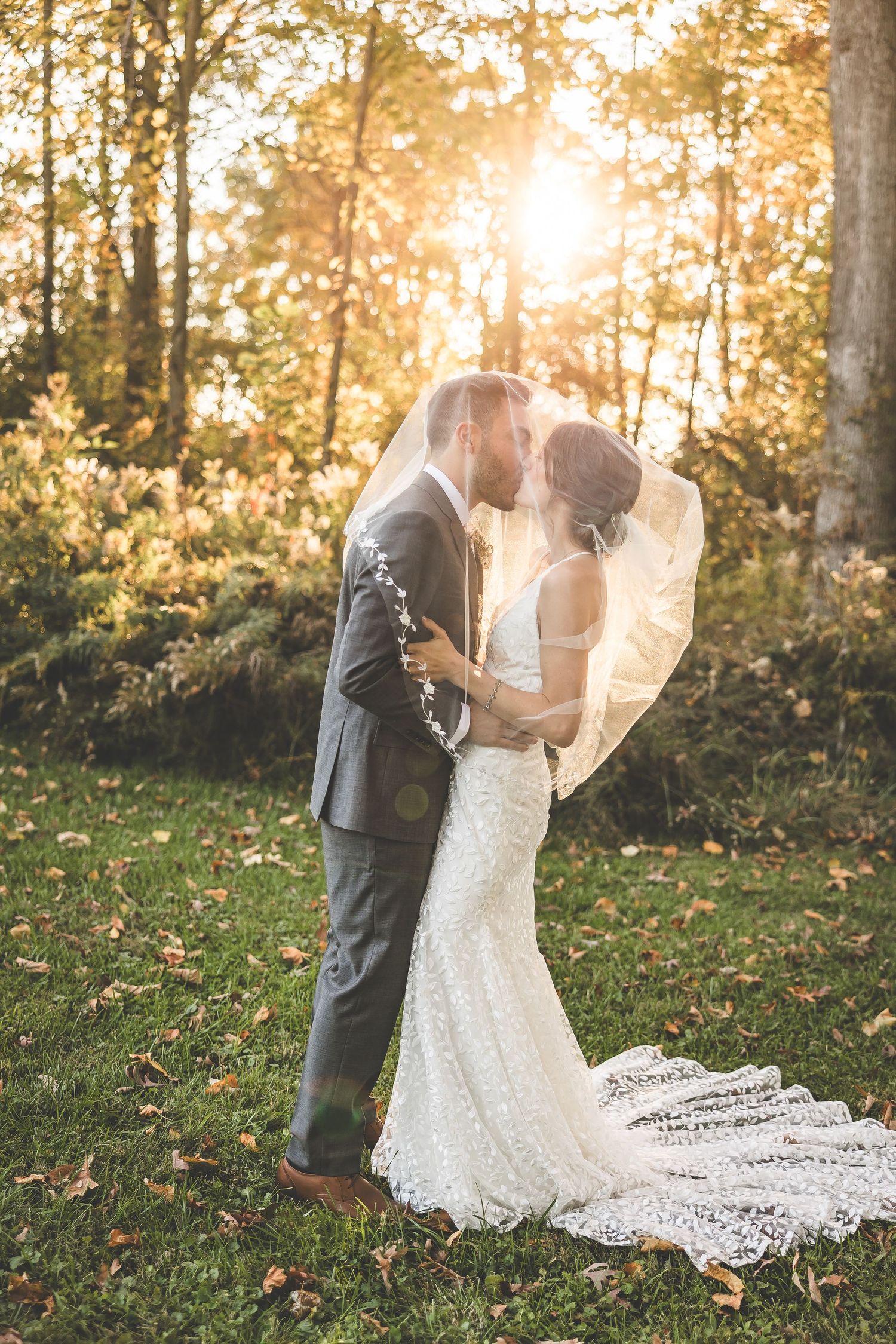 Elegant wedding portrait with flowing veil in autumn forest setting.