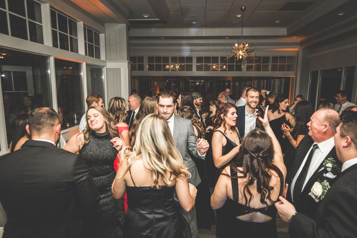 Crowded dance floor at a wedding reception with guests in formal attire dancing under ambient lighting.
