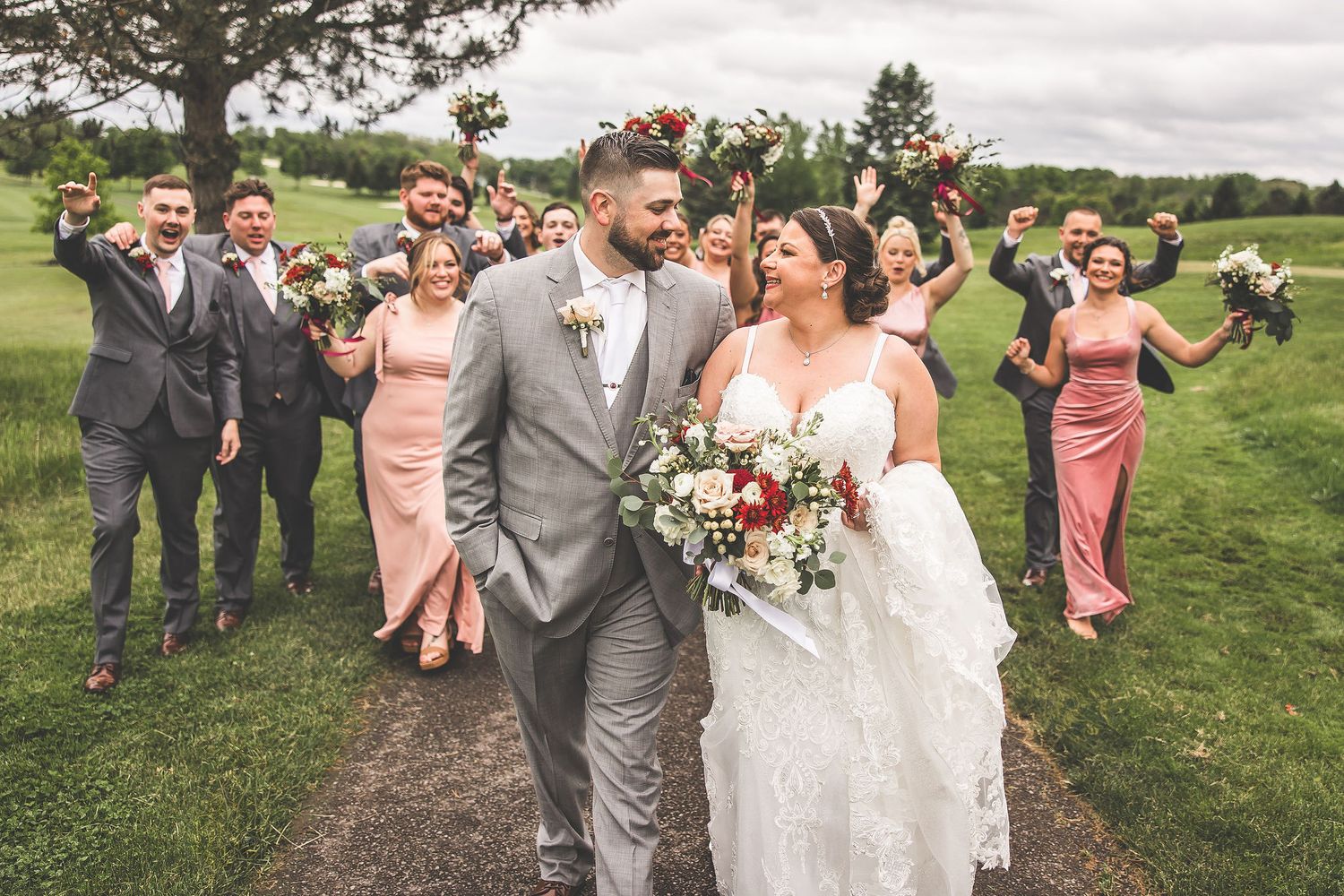 Wedding party members gather outdoors for group photos in pink and gray attire.