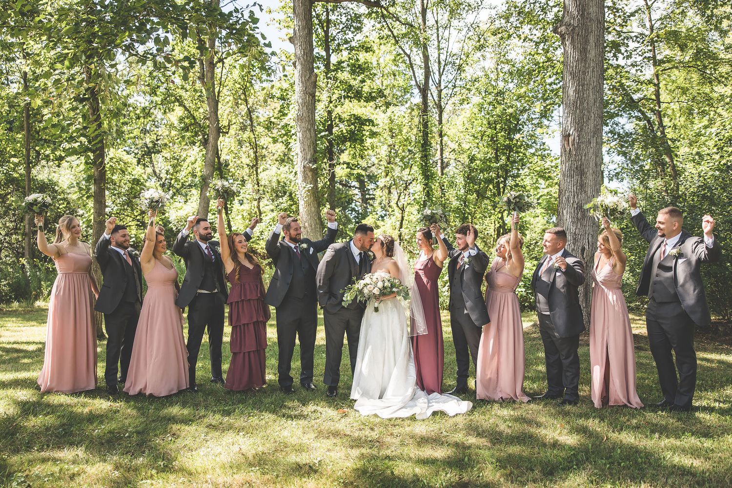 Wedding party poses in a line outdoors with bridesmaids in pink gowns and groomsmen in suits.