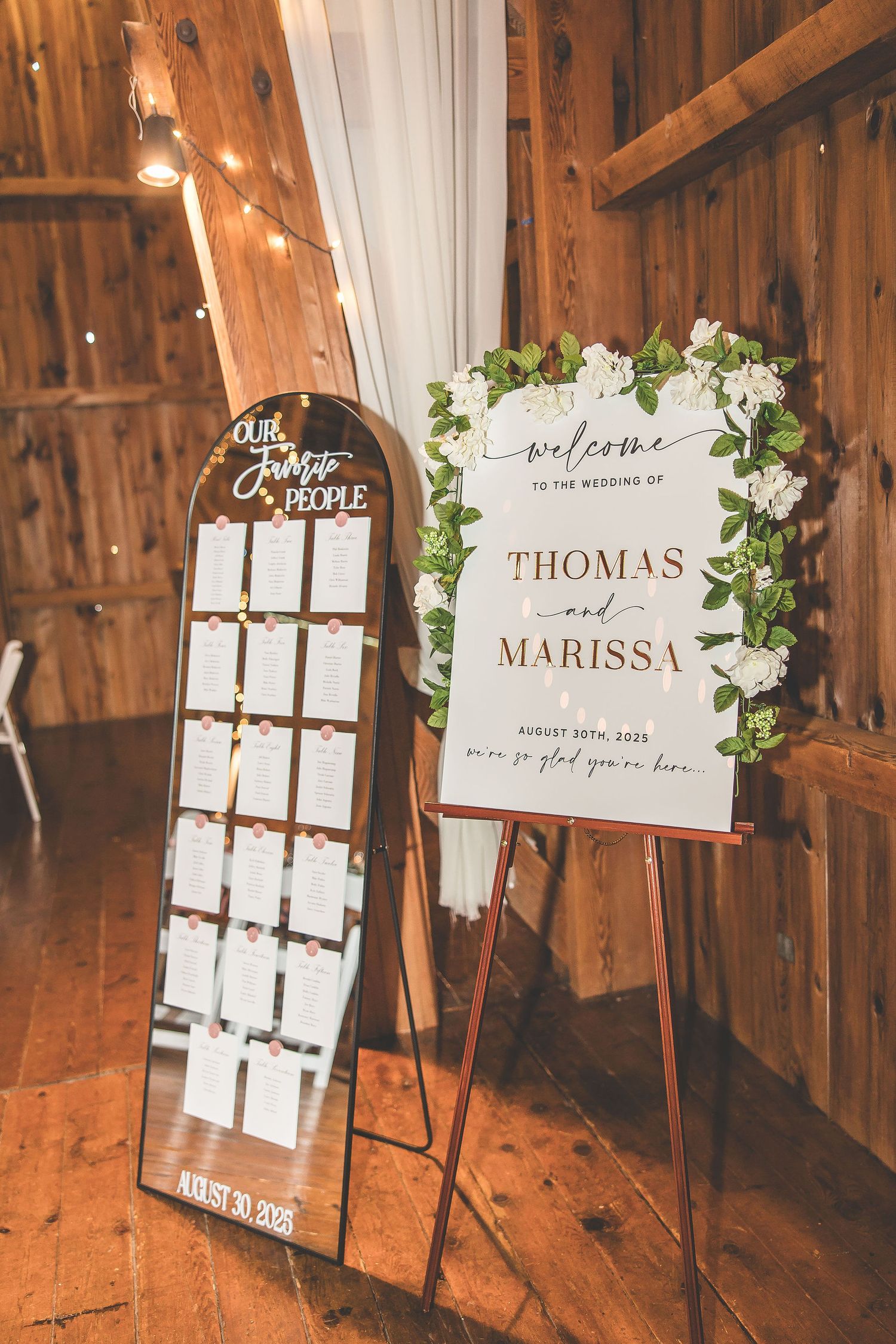 Wedding seating chart and welcome sign displayed on easels in rustic barn venue.