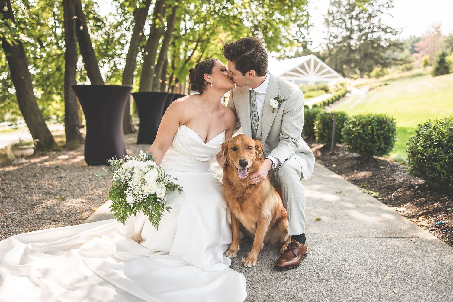 A couple kneels with their happy golden retriever during outdoor wedding portraits.