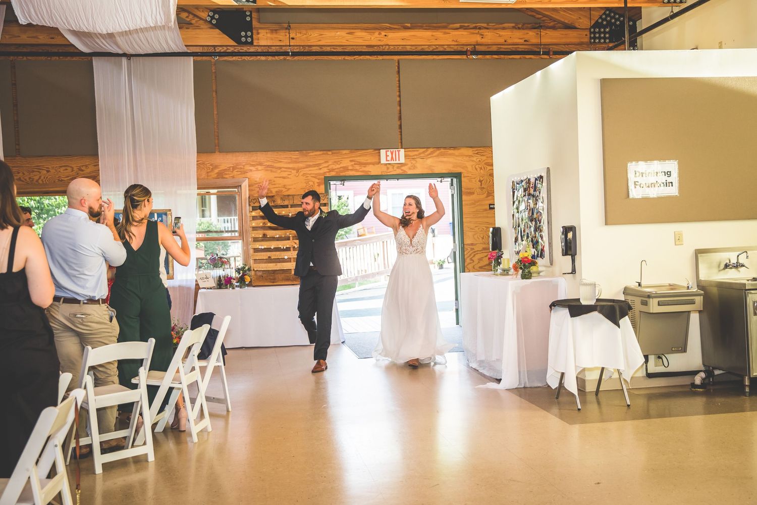 Wedding celebration in a rustic venue with guests celebrating and white folding chairs.