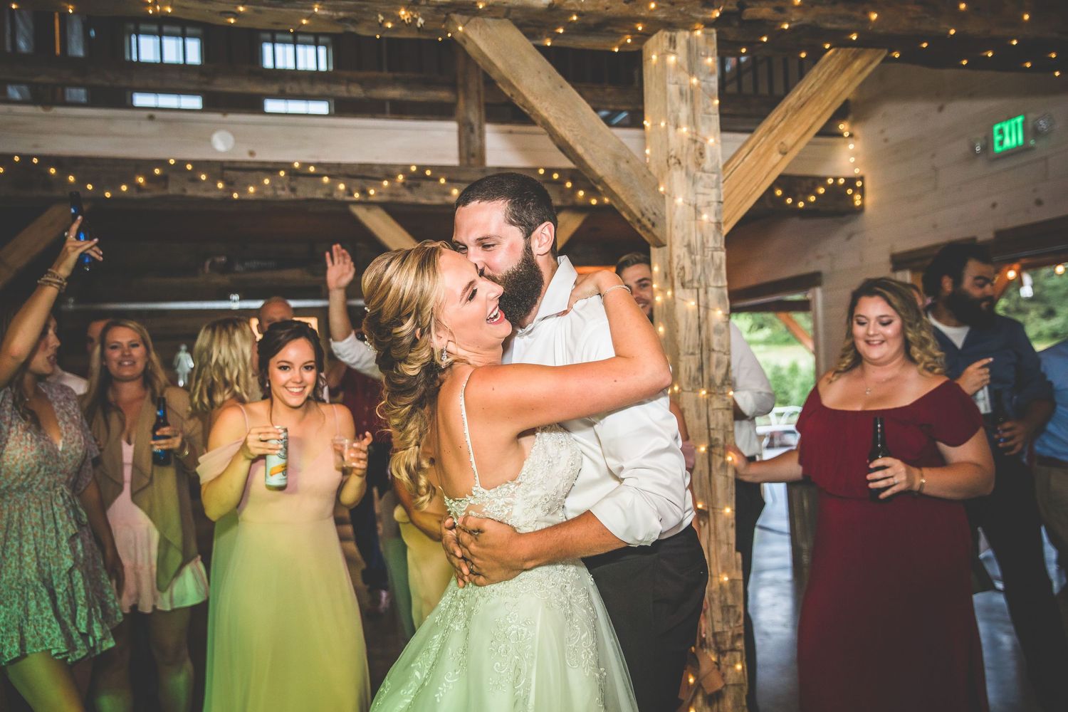 Wedding party dancing and celebrating in a barn decorated with string lights.