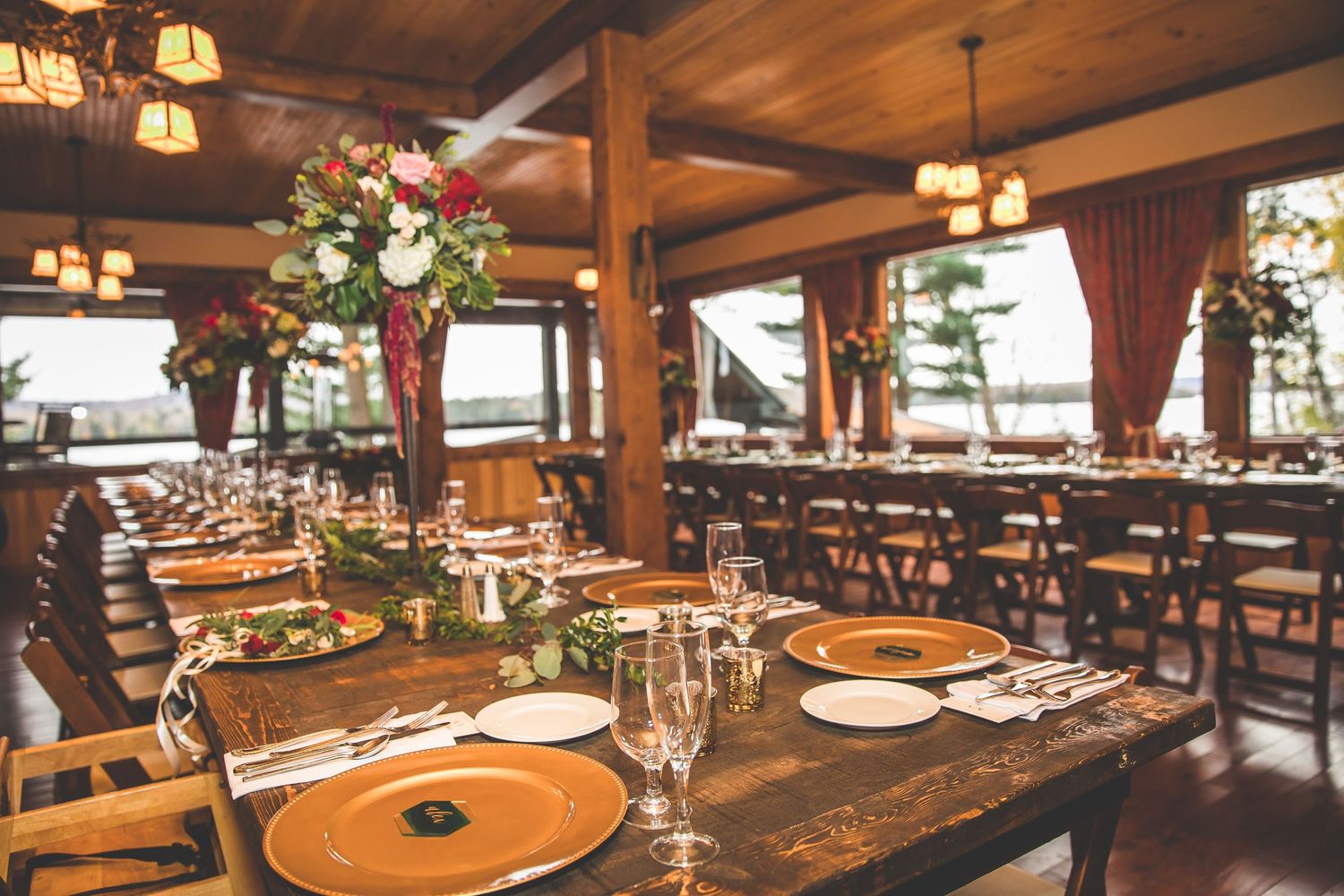 Rustic wooden lodge dining room with round tables set for an elegant event under warm lighting.