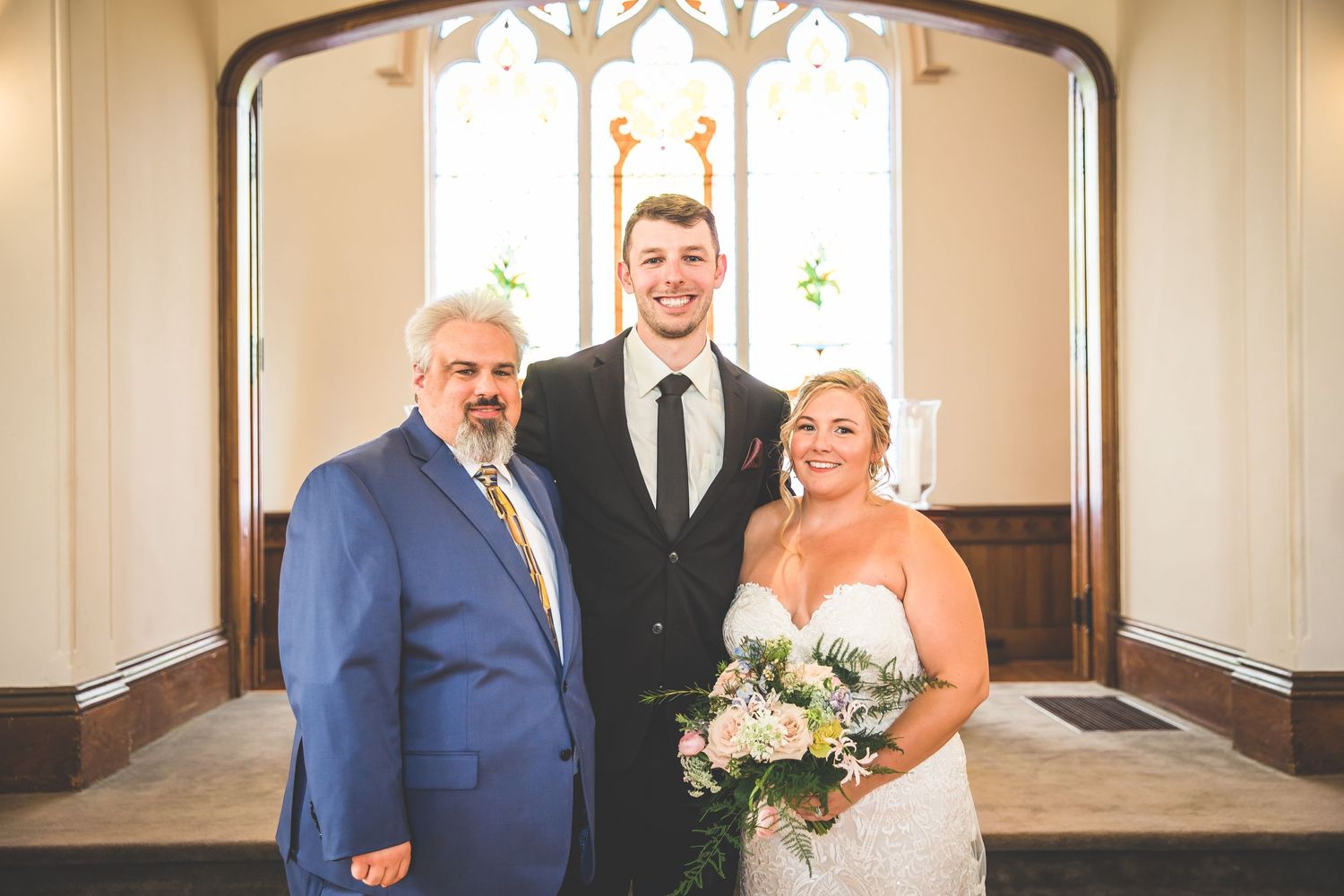 Wedding portrait in front of a church's stained glass window with elegant lighting.