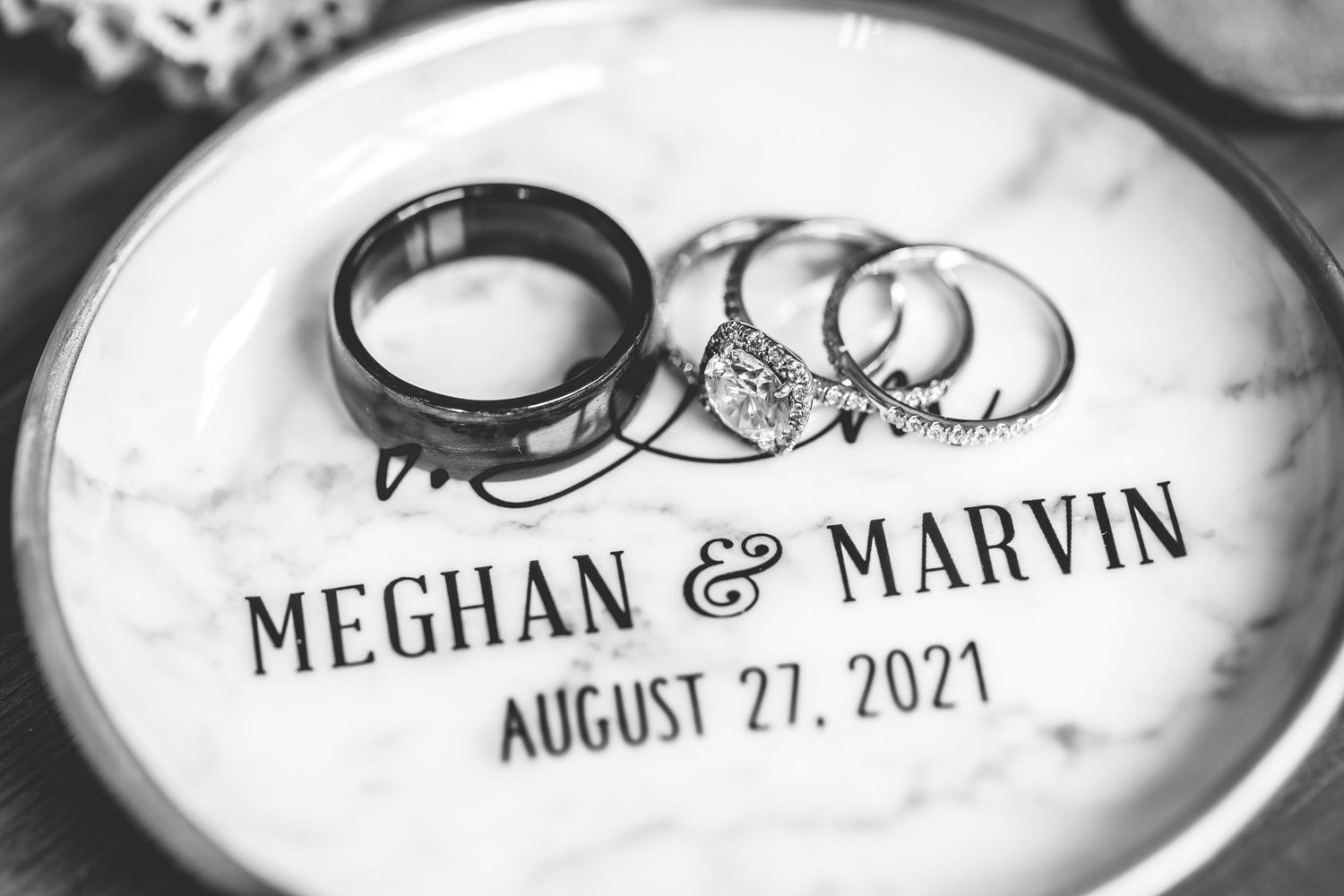 Wedding rings and couple's names Meghan & Marvin engraved on white ceramic plate.