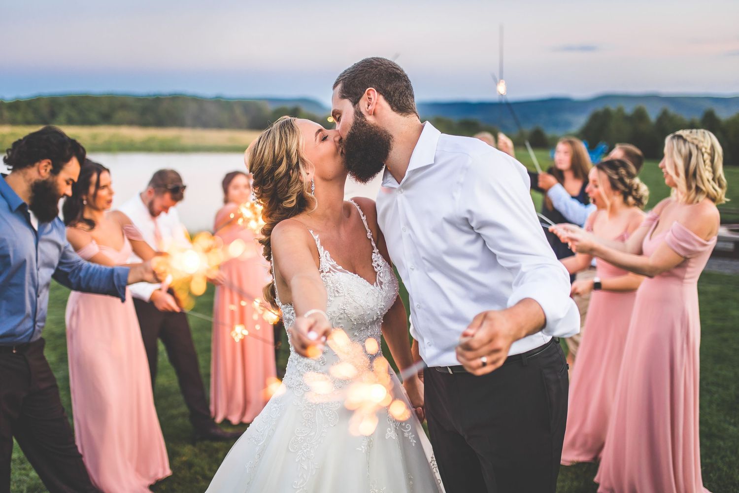 A couple dances outdoors at sunset surrounded by bridesmaids in pink dresses.