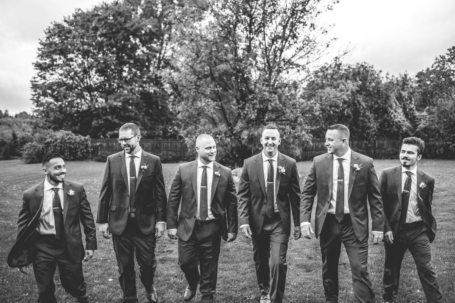 Black and white photo of groomsmen in formal attire posing together outdoors.