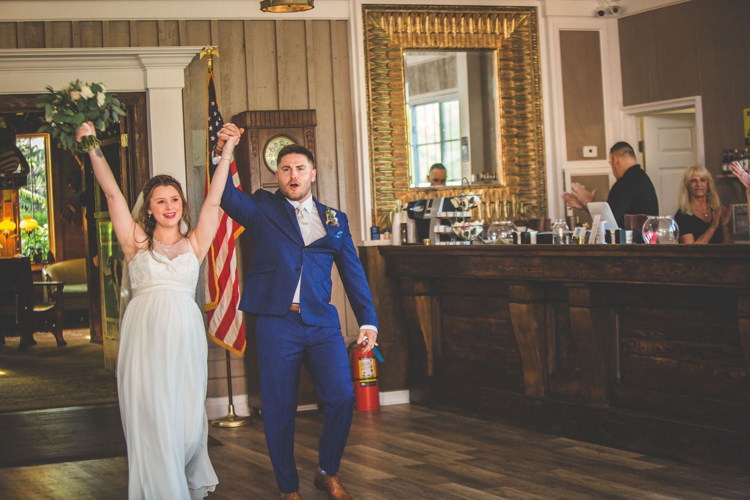 Newlyweds making their grand entrance into their reception venue with raised hands in celebration.
