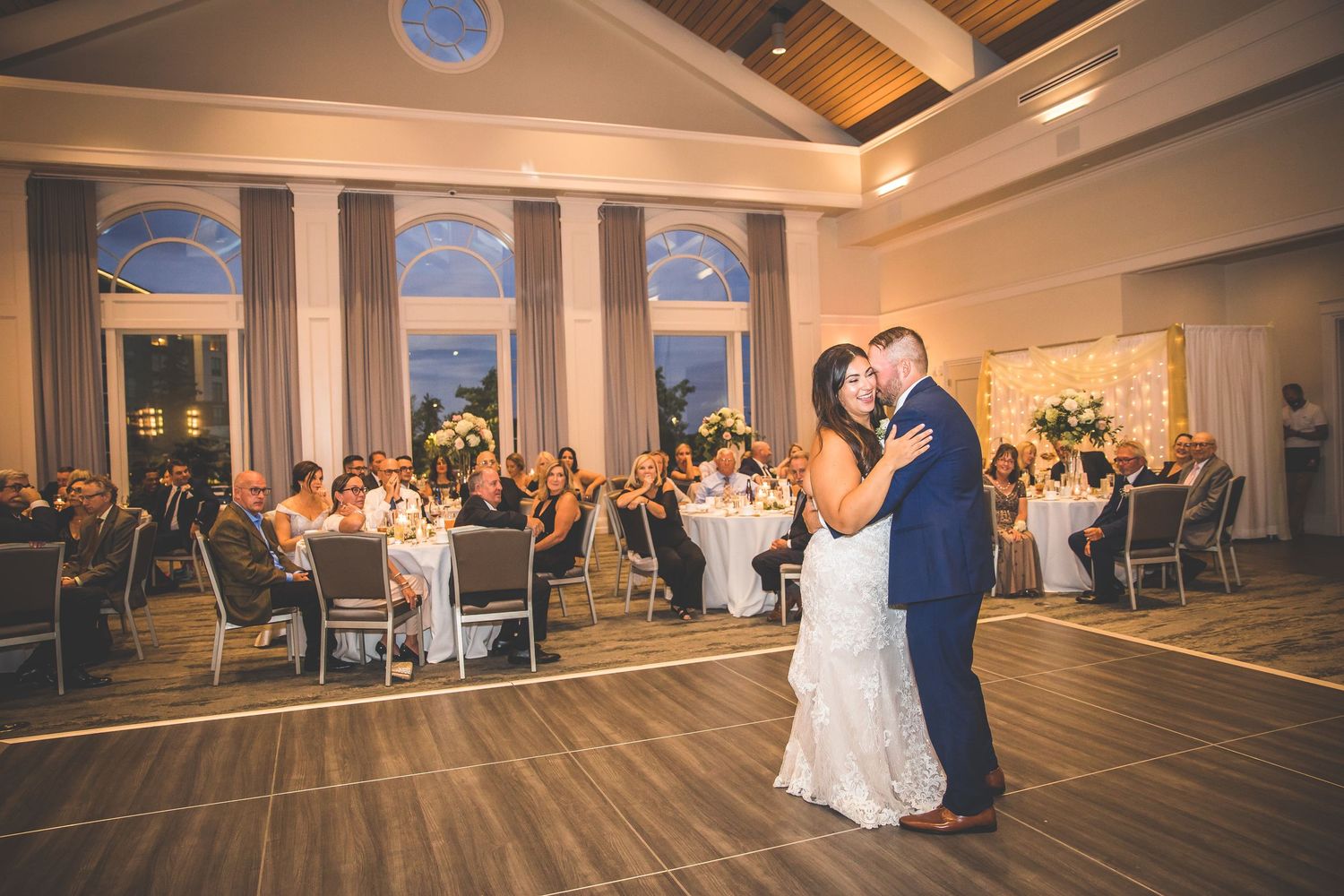 Spacious wedding reception ballroom with white decor and ambient lighting.