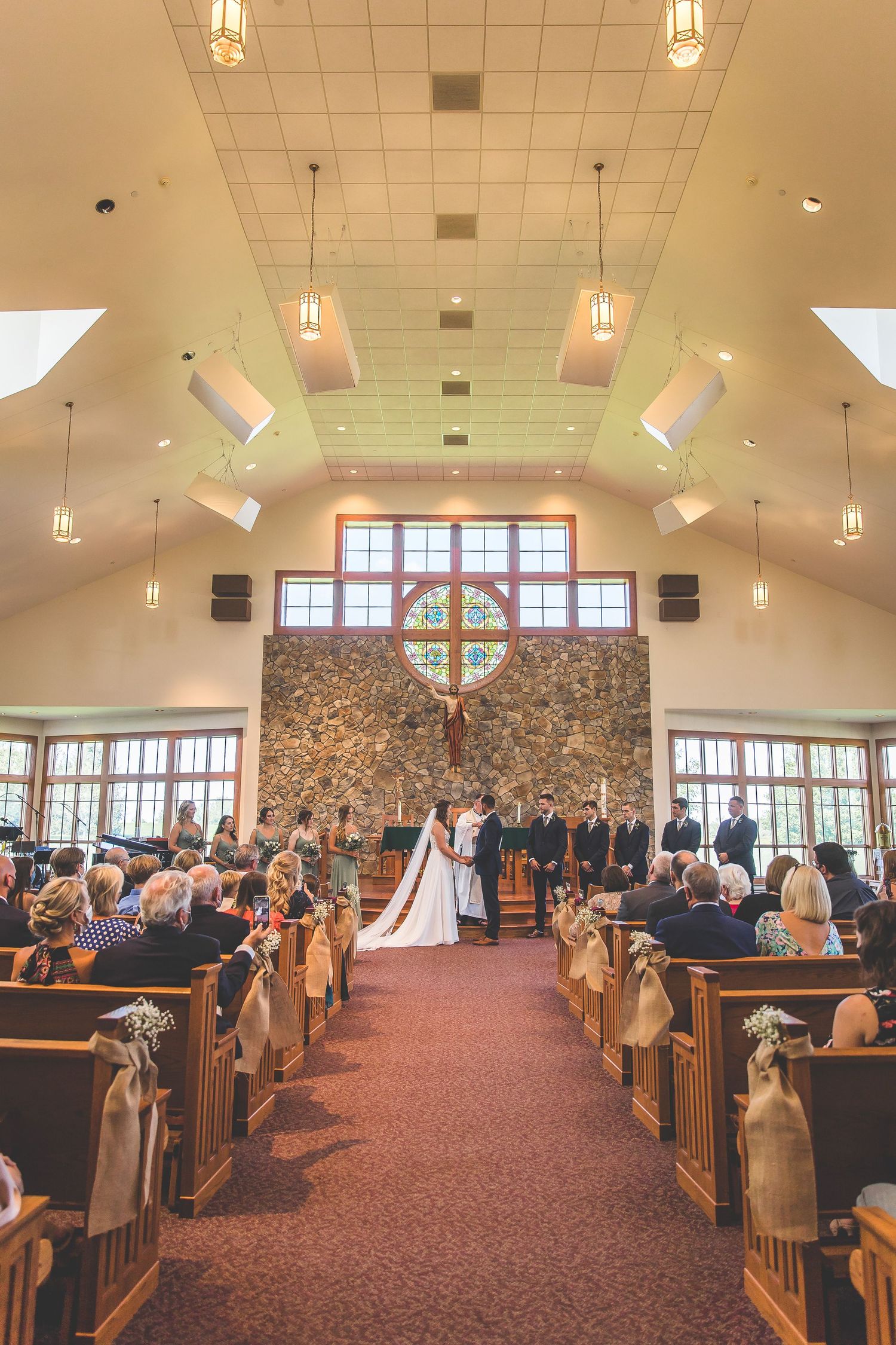 Interior views of a church sanctuary with vaulted ceilings and pendant lighting during a wedding.