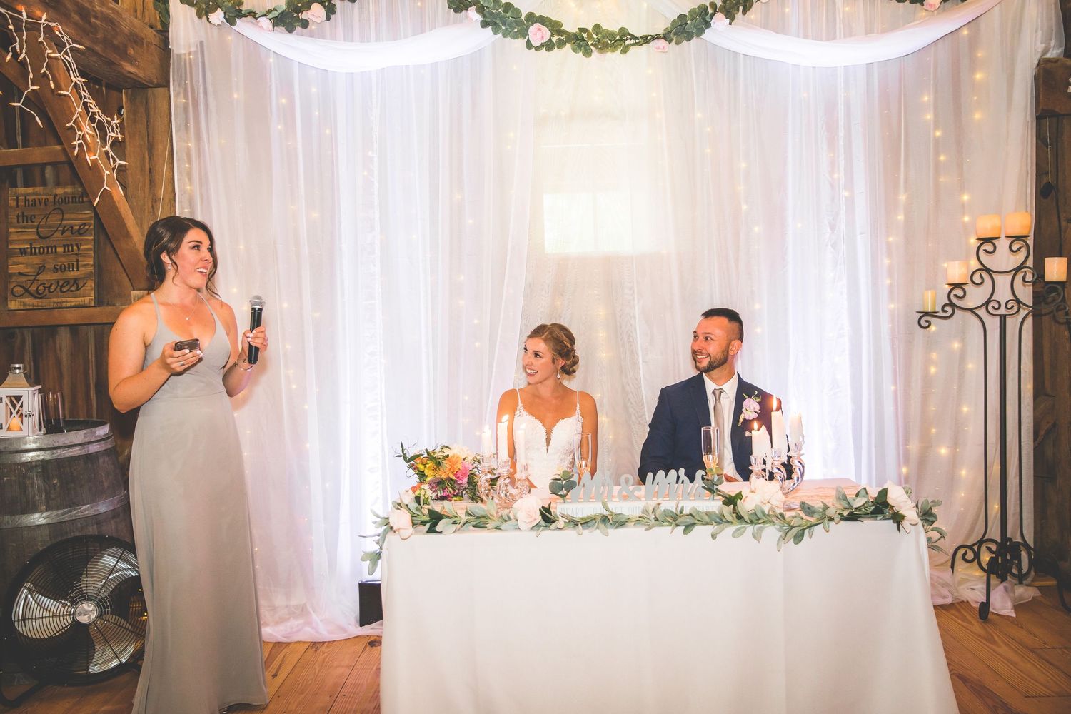 Rustic barn wedding reception setup with elegant white draping and floral garlands.