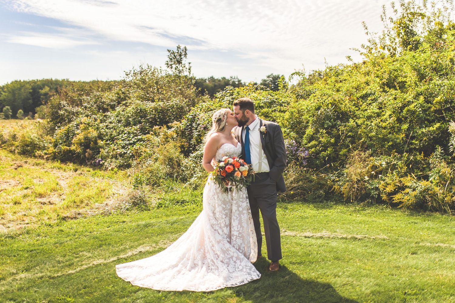 Wedding couple shares romantic moments in a sunny meadow with rolling hills in background.