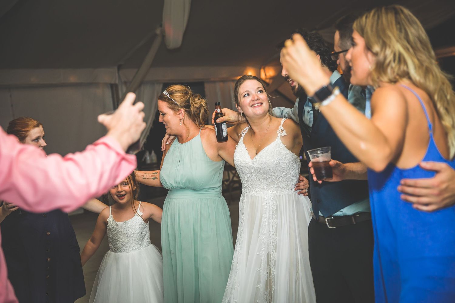 A group of people in formal attire dancing and singing together at a reception.