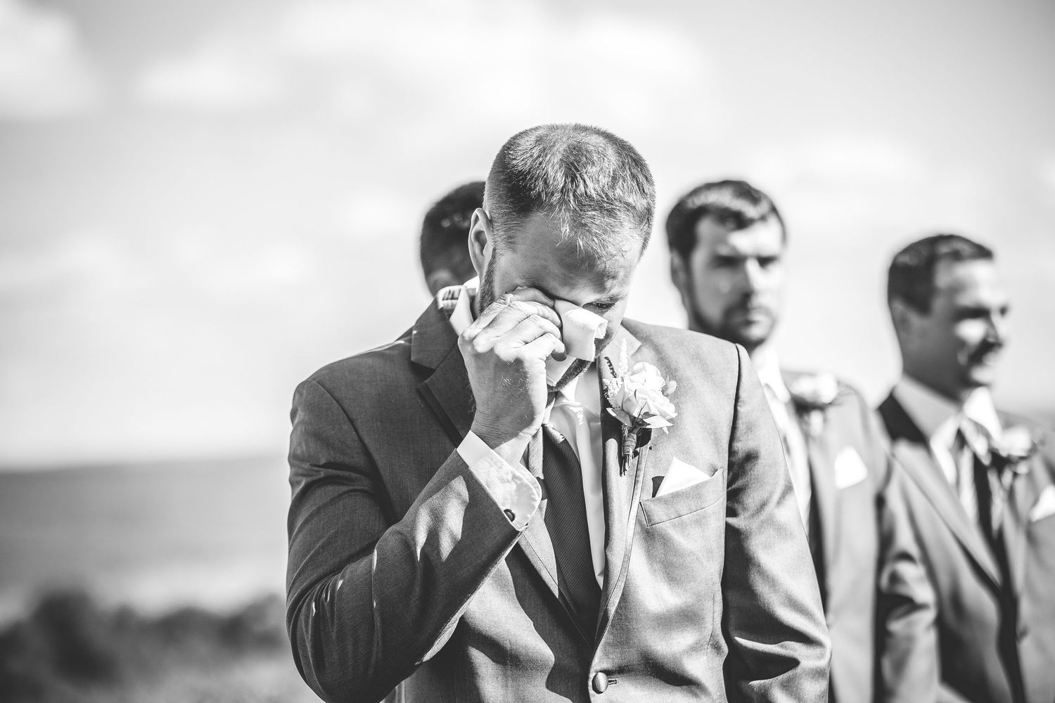 Wedding party members in gray suits sharing emotional moments outdoors.