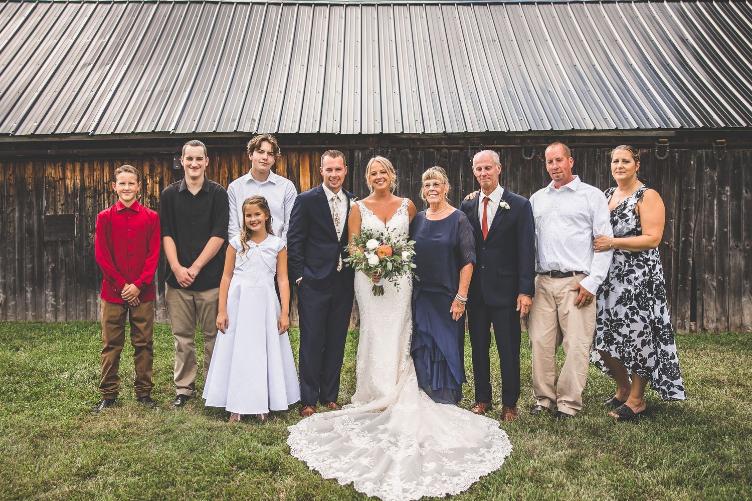Extended family and wedding party members pose together for a group photo outdoors.