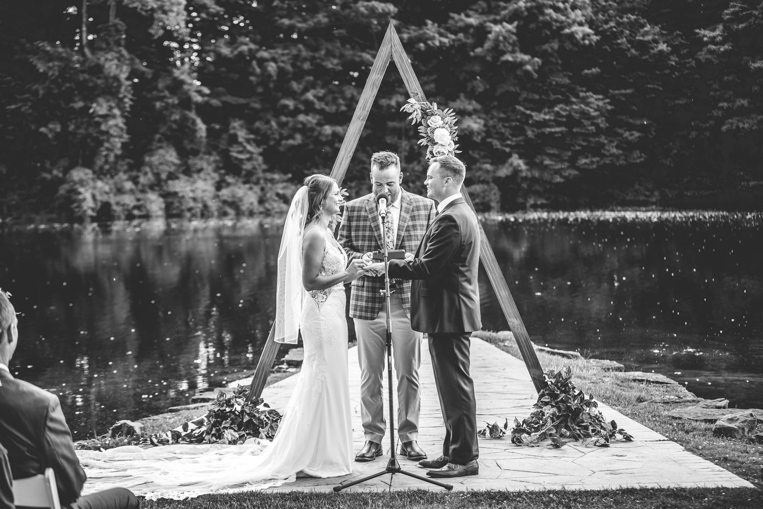 Rustic outdoor wedding ceremony setup with wooden triangle arch and white chairs.