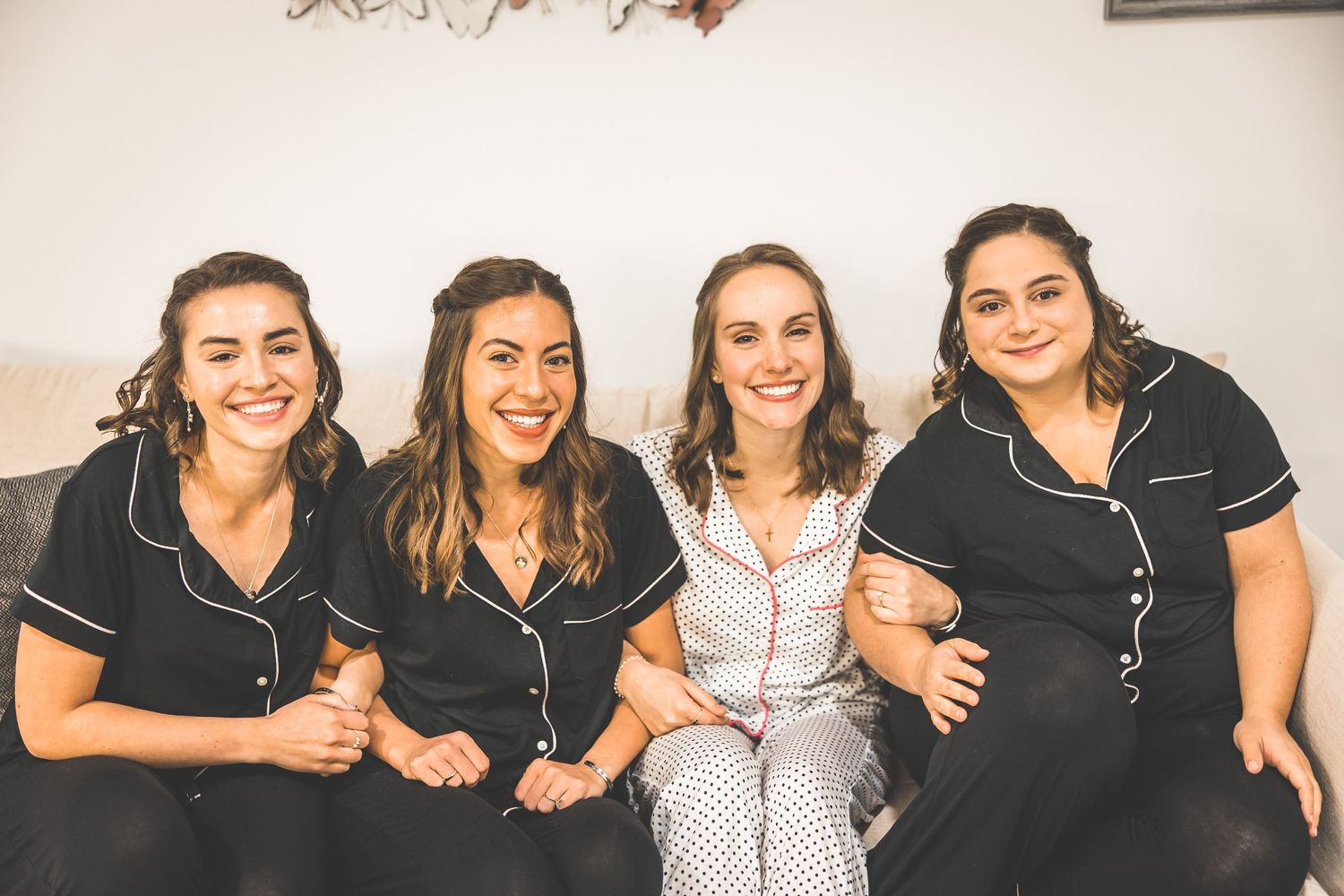 Friends pose together in casual attire against white wall.