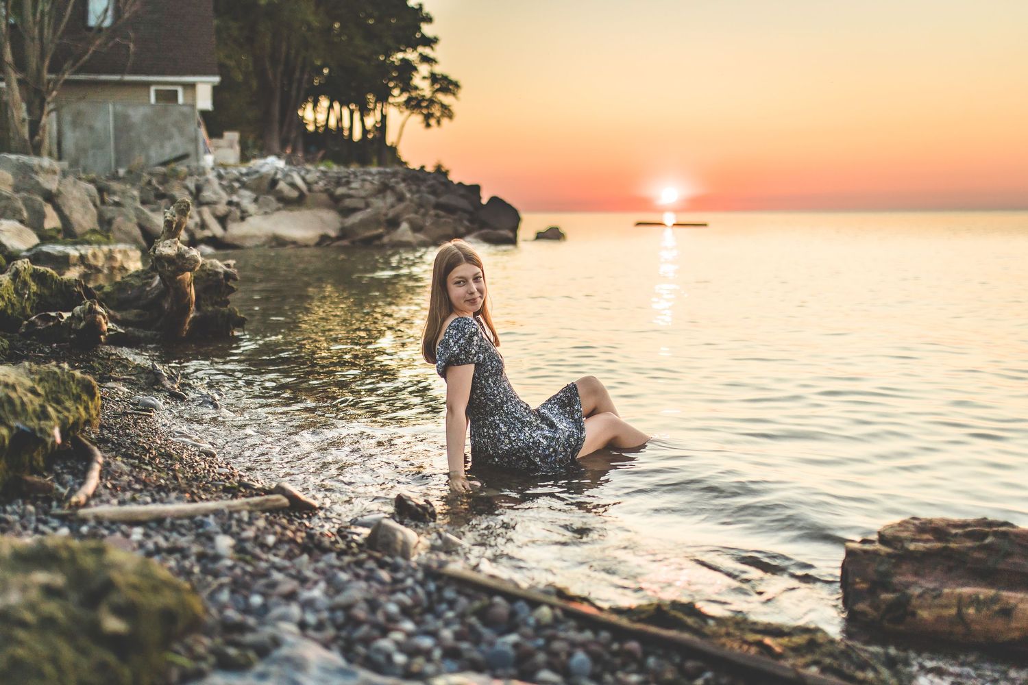 Beautiful sunset engagement session along a rocky shoreline with golden light reflecting on the water.