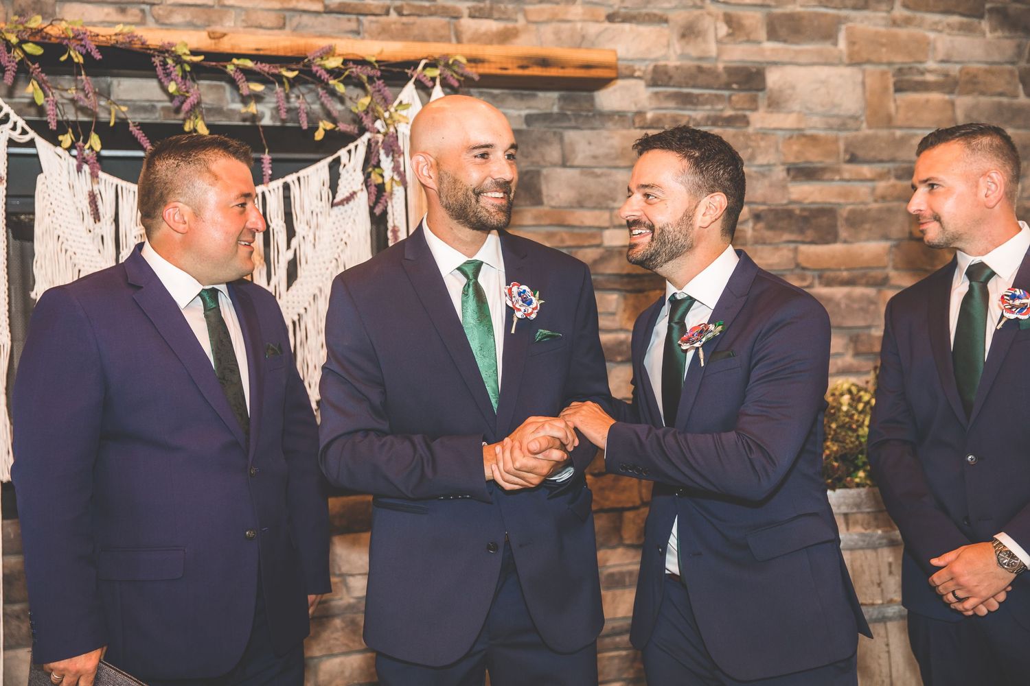 Groomsmen in navy suits standing against rustic stone wall backdrop.