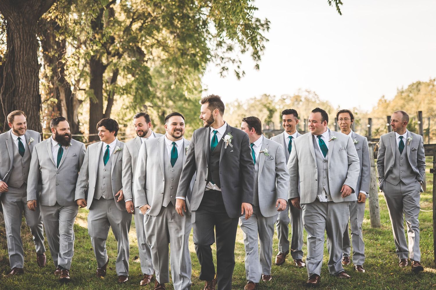Wedding party in gray suits walks together across a grassy field during golden hour.