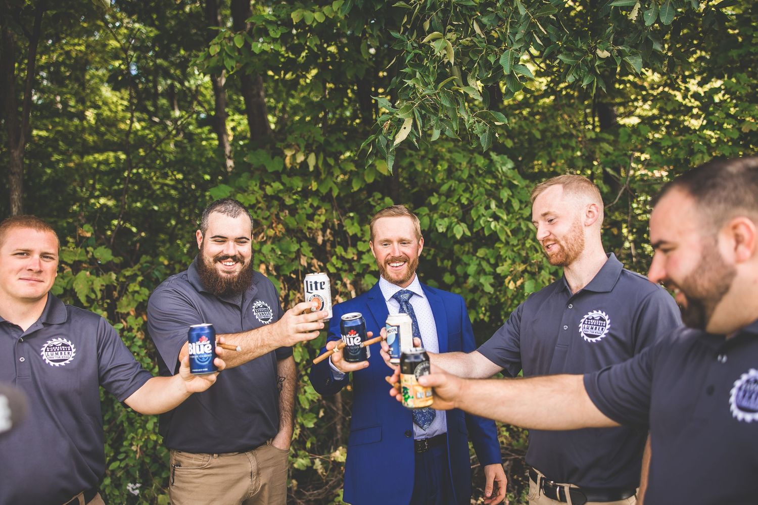 Groomsmen in matching dark uniforms share drinks and laughs outdoors during a wedding celebration.