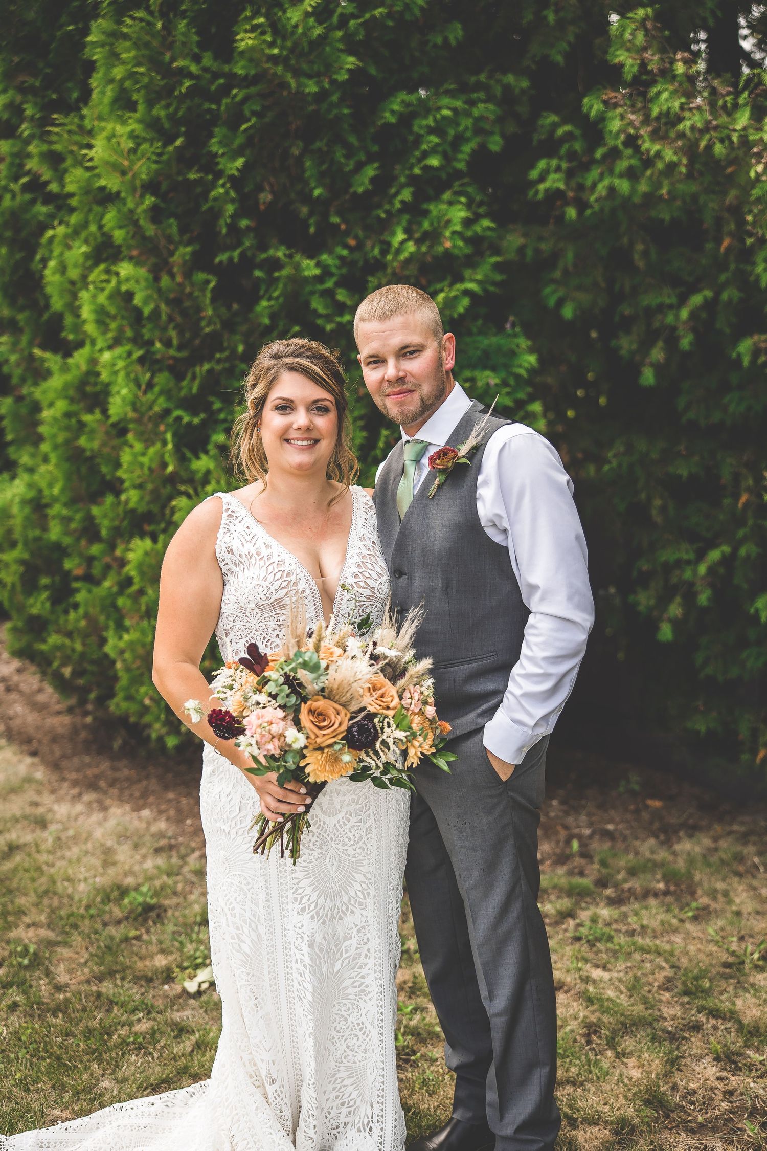 Wedding party members pose for casual photos in front of lush greenery.