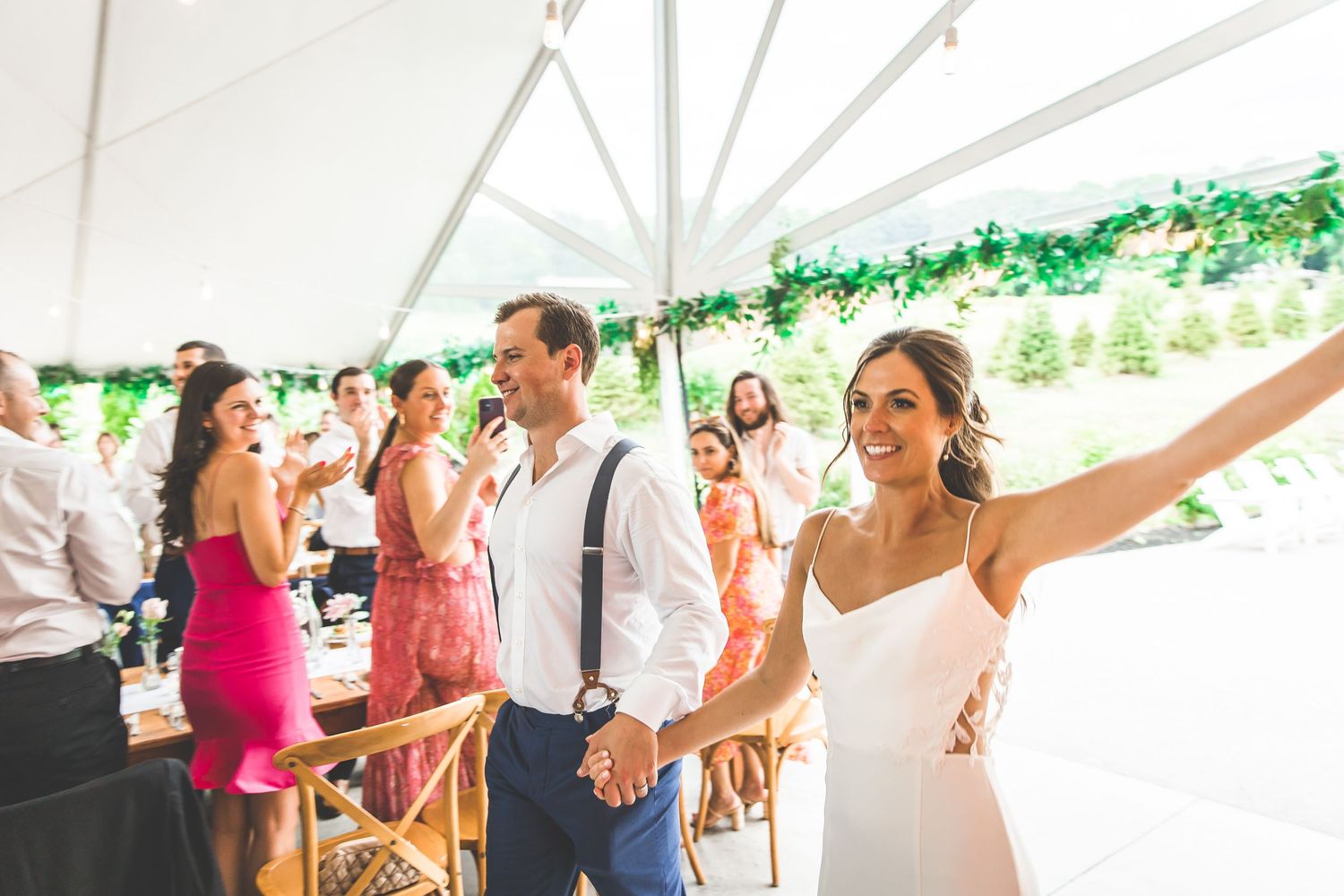 Wedding reception party guests dancing and celebrating under a white tent with green decorations.