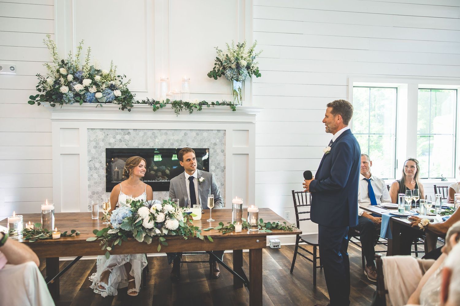Elegant wedding reception venue decorated with white floral arrangements and greenery.