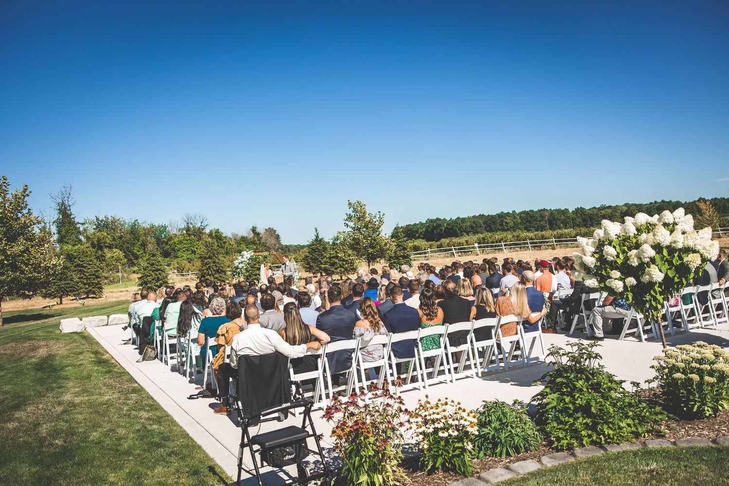 Panoramic view of wedding ceremony setup with white chairs and floral arrangements against blue sky.
