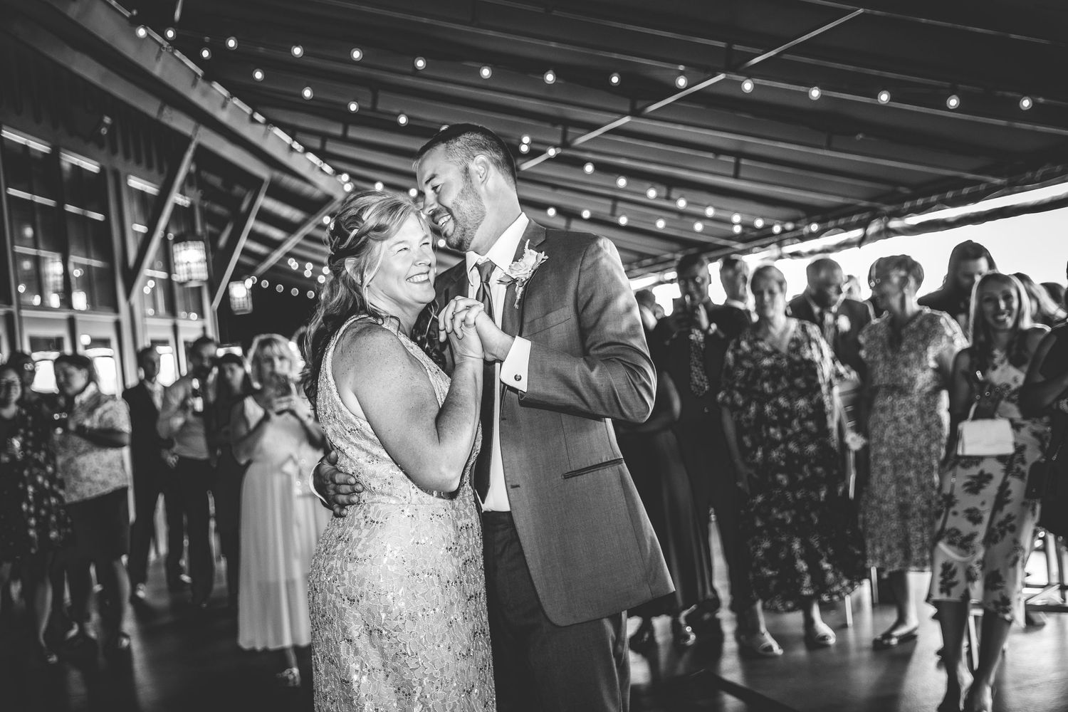 Wedding reception panorama showing guests dancing under string lights in an indoor venue.