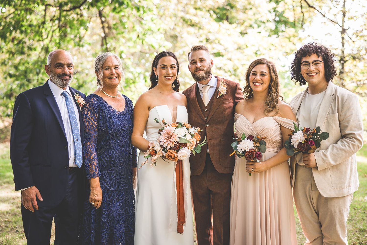 Wedding party members stand together in navy and neutral colors against a natural backdrop.