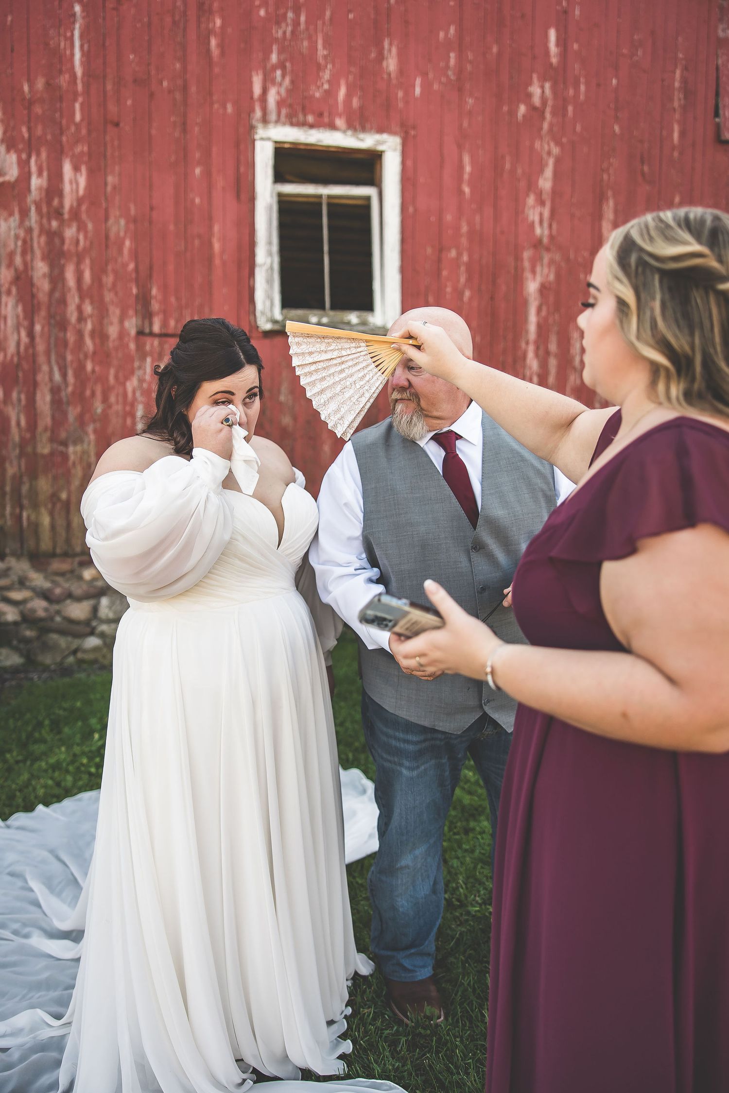 Wedding party celebrates with fans during outdoor barn photoshoot.