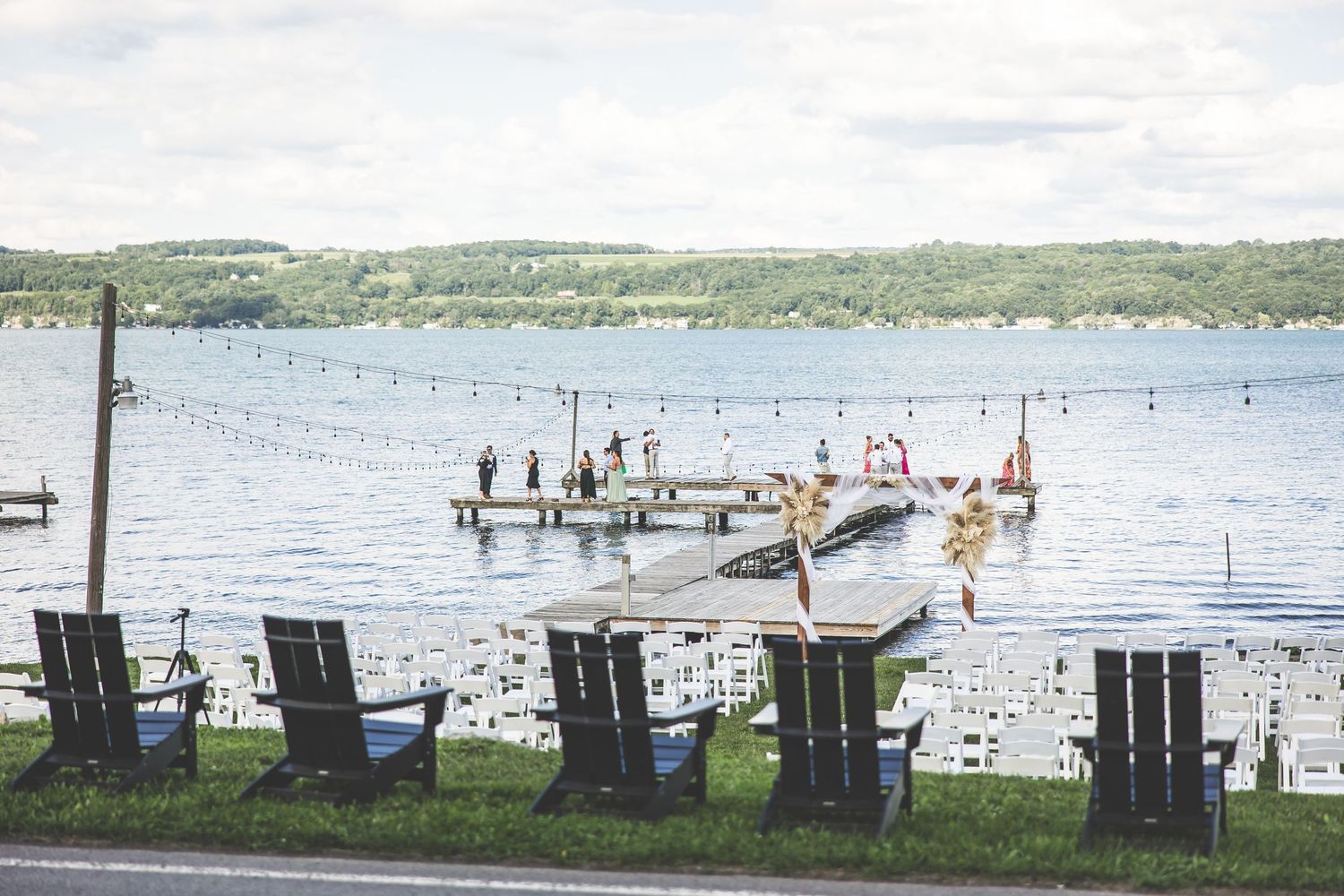 Row of black Adirondack chairs lined up along a waterfront dock with scenic lake views.