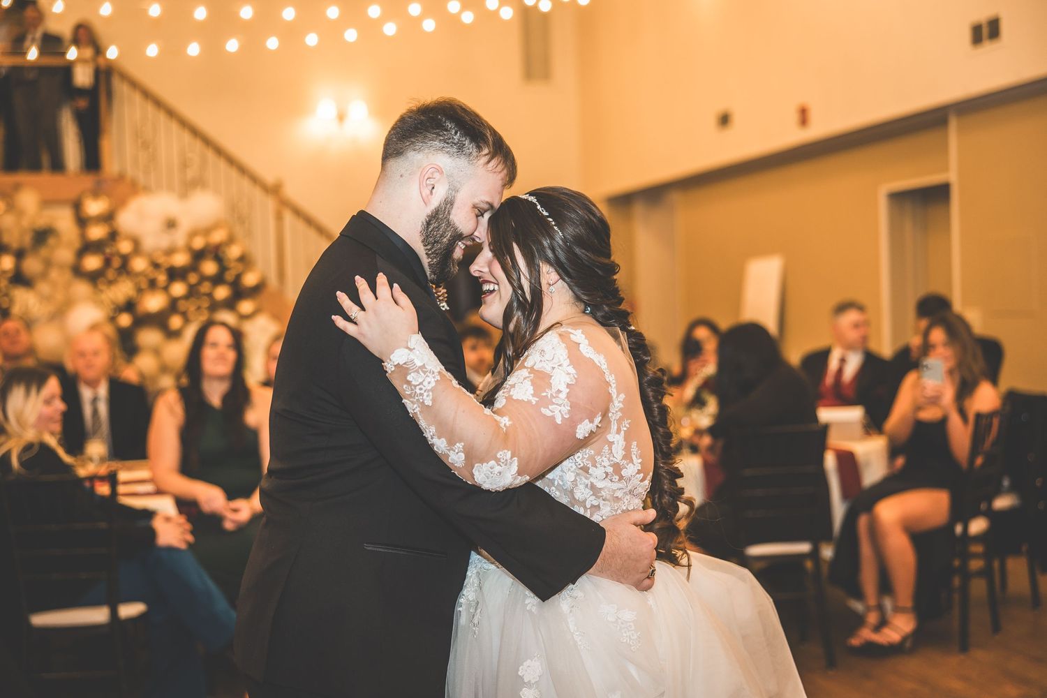 First dance at wedding reception under warm glowing string lights with guests watching.