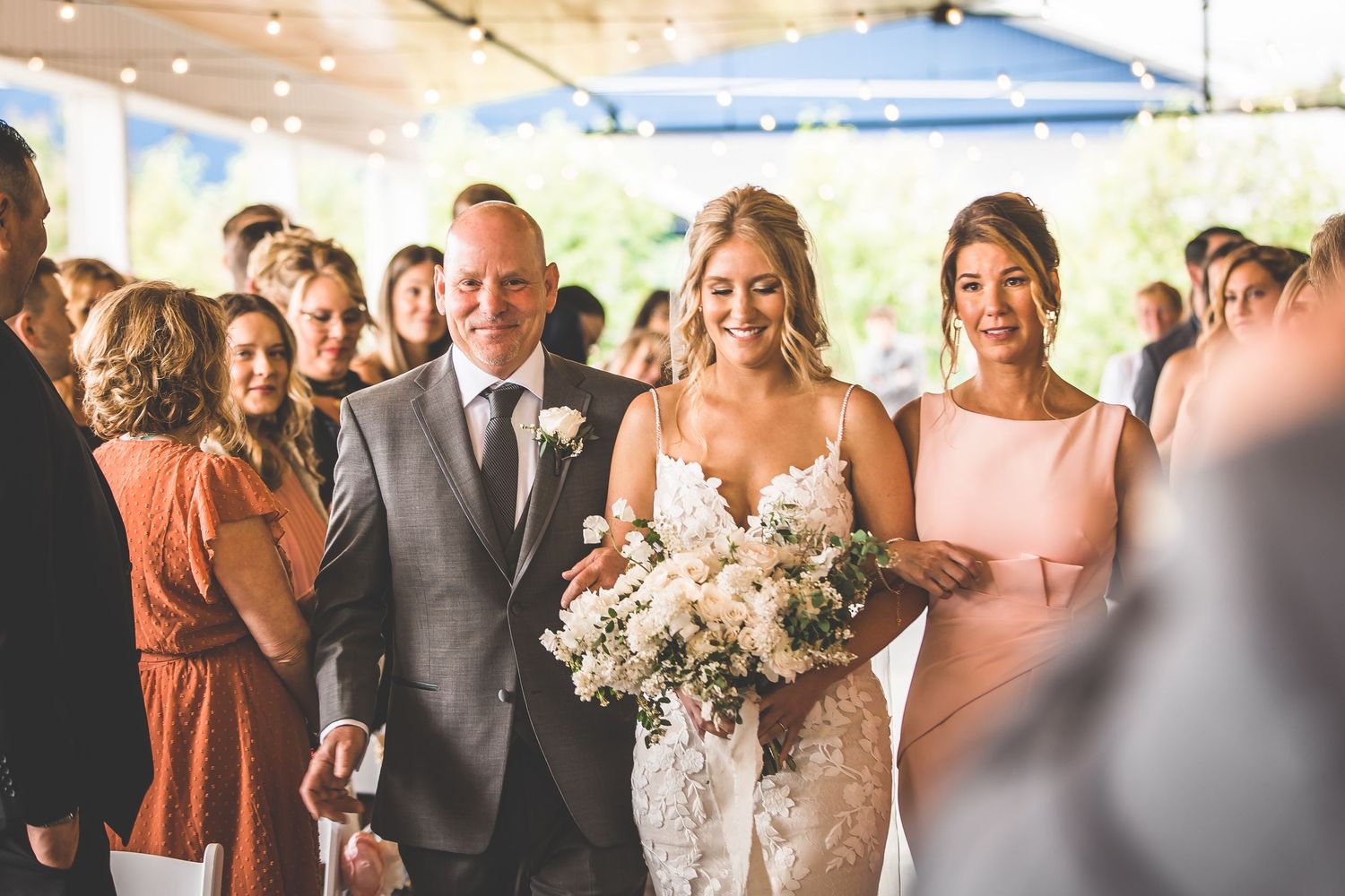 Wedding processional in bright venue with bride carrying white floral bouquet.