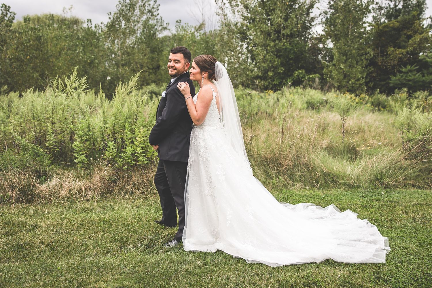 A flowing white wedding dress train spreads across green grass in an outdoor garden setting.