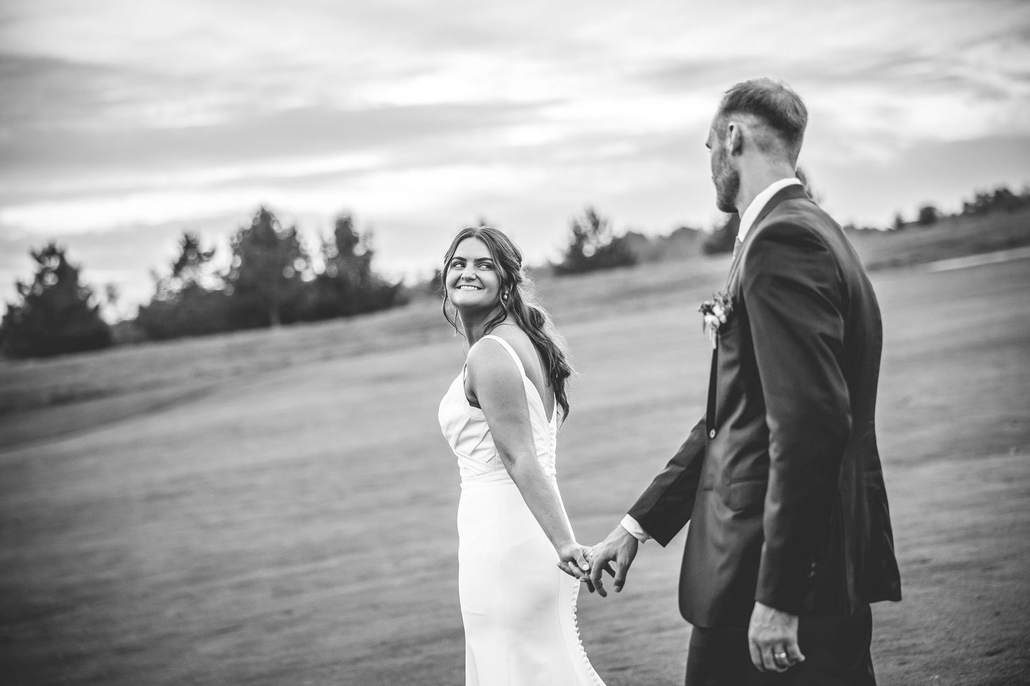 Wedding couple posing in a scenic field at golden hour with dramatic sky.