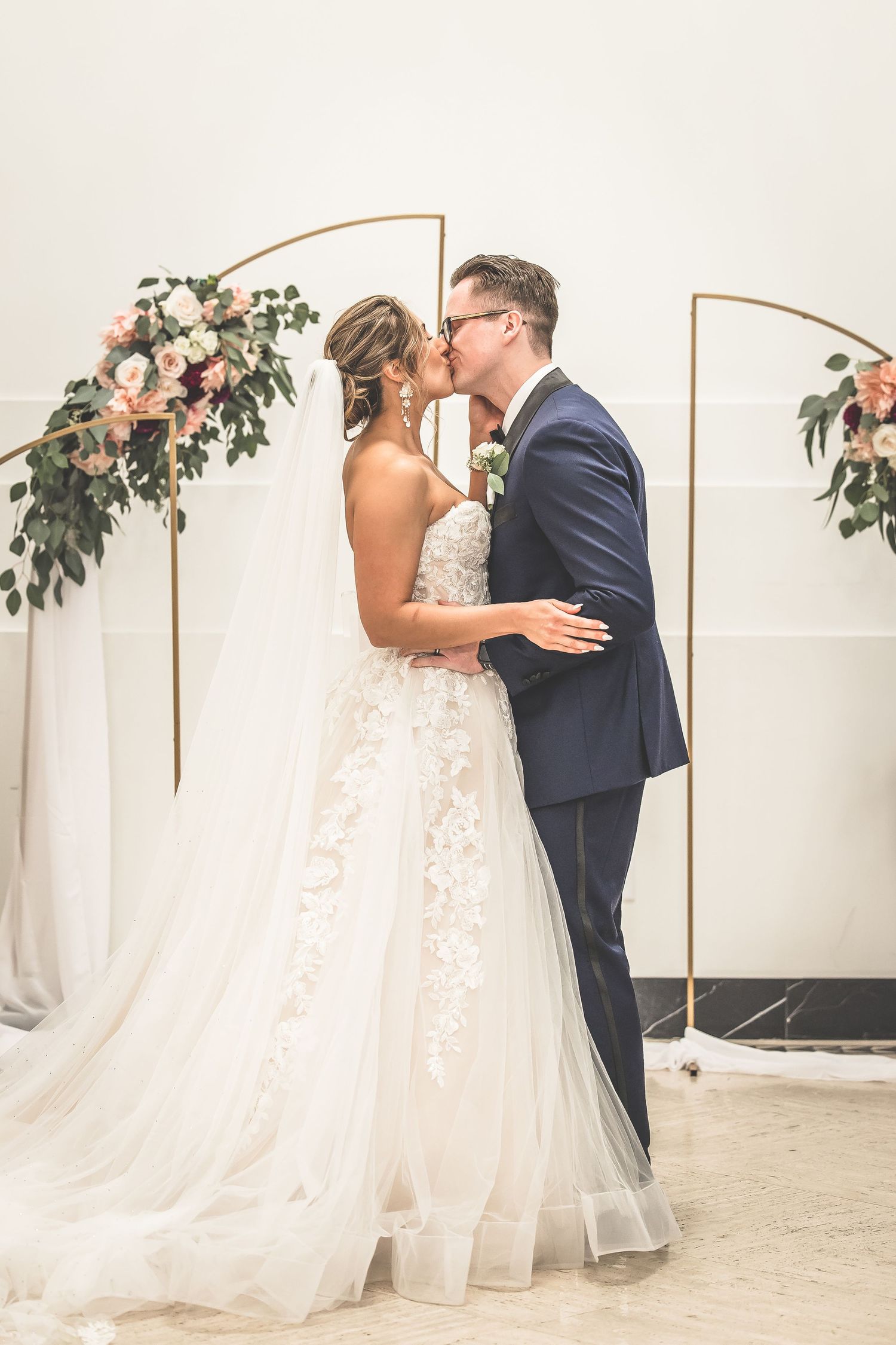 Emotional wedding ceremony exchange under copper arch with floral decorations.