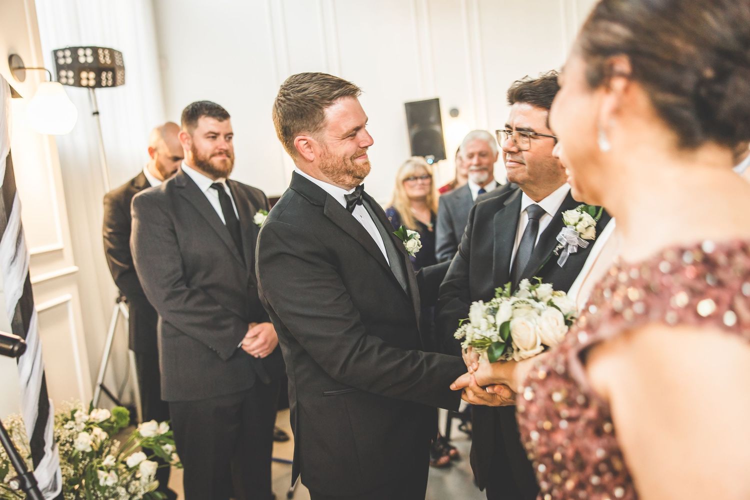 Wedding party members mingle during reception in elegant venue with floral decorations.
