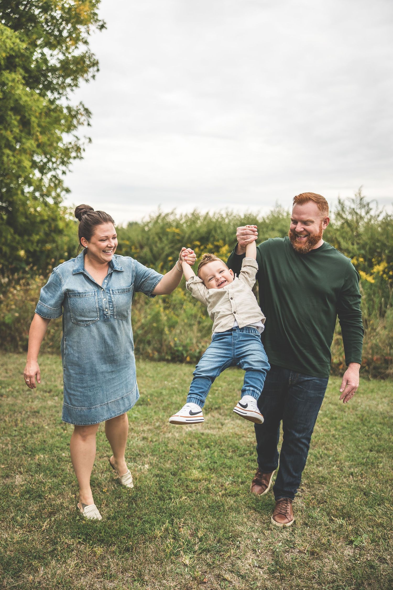 A playful family swinging and lifting a small child between them on a grassy hill.