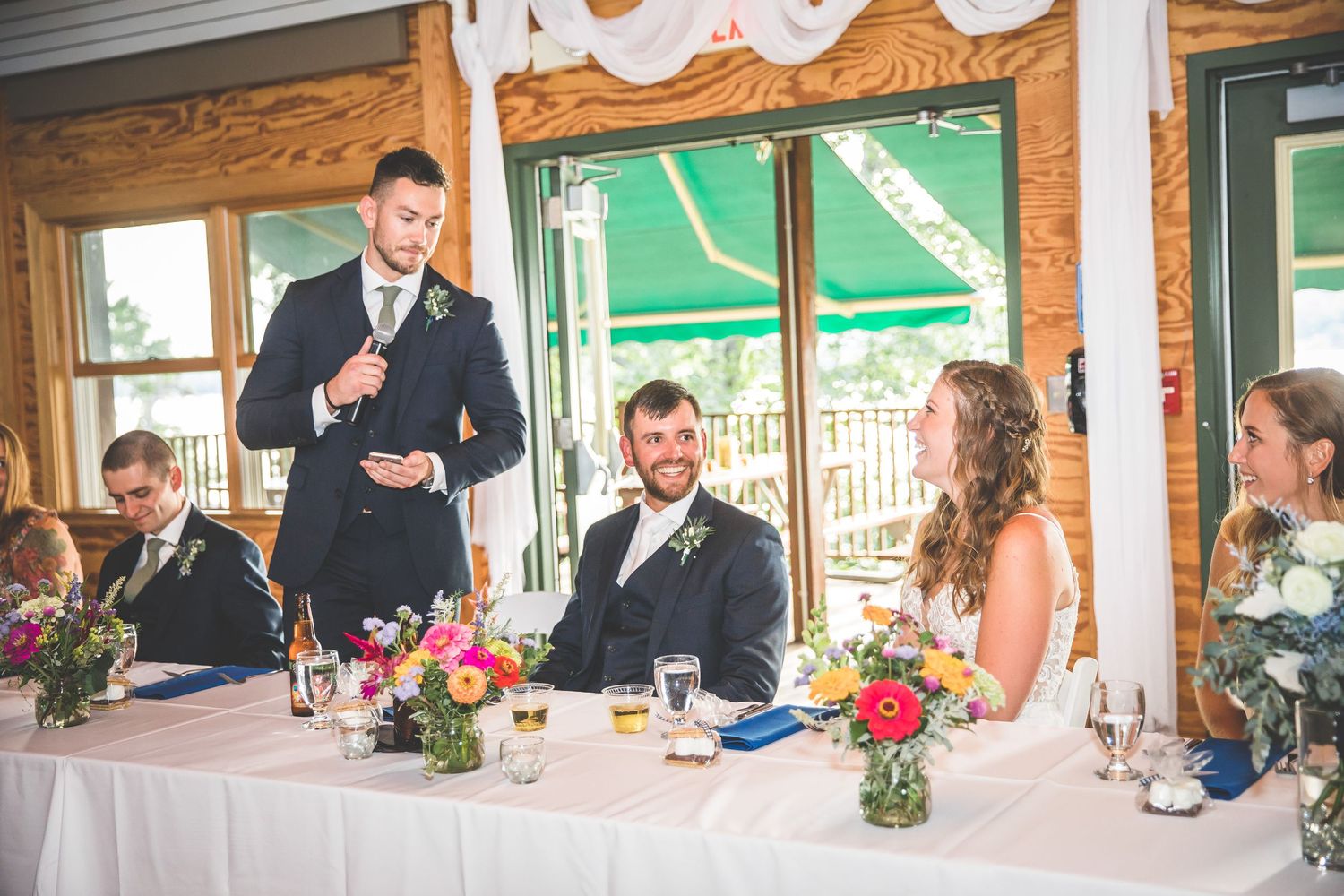 Wedding reception tables set in rustic venue with wooden walls and green accents.