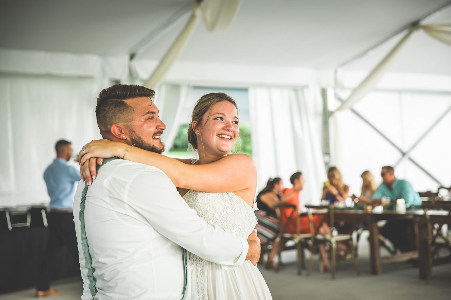 Wedding reception candid moments captured under an elegant white tent with chandeliers.